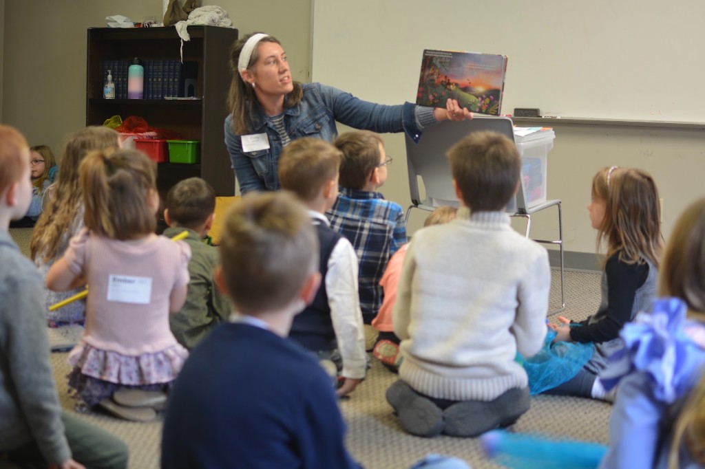 A teacher shows a picture book to young children sitting on the floor during children’s ministry